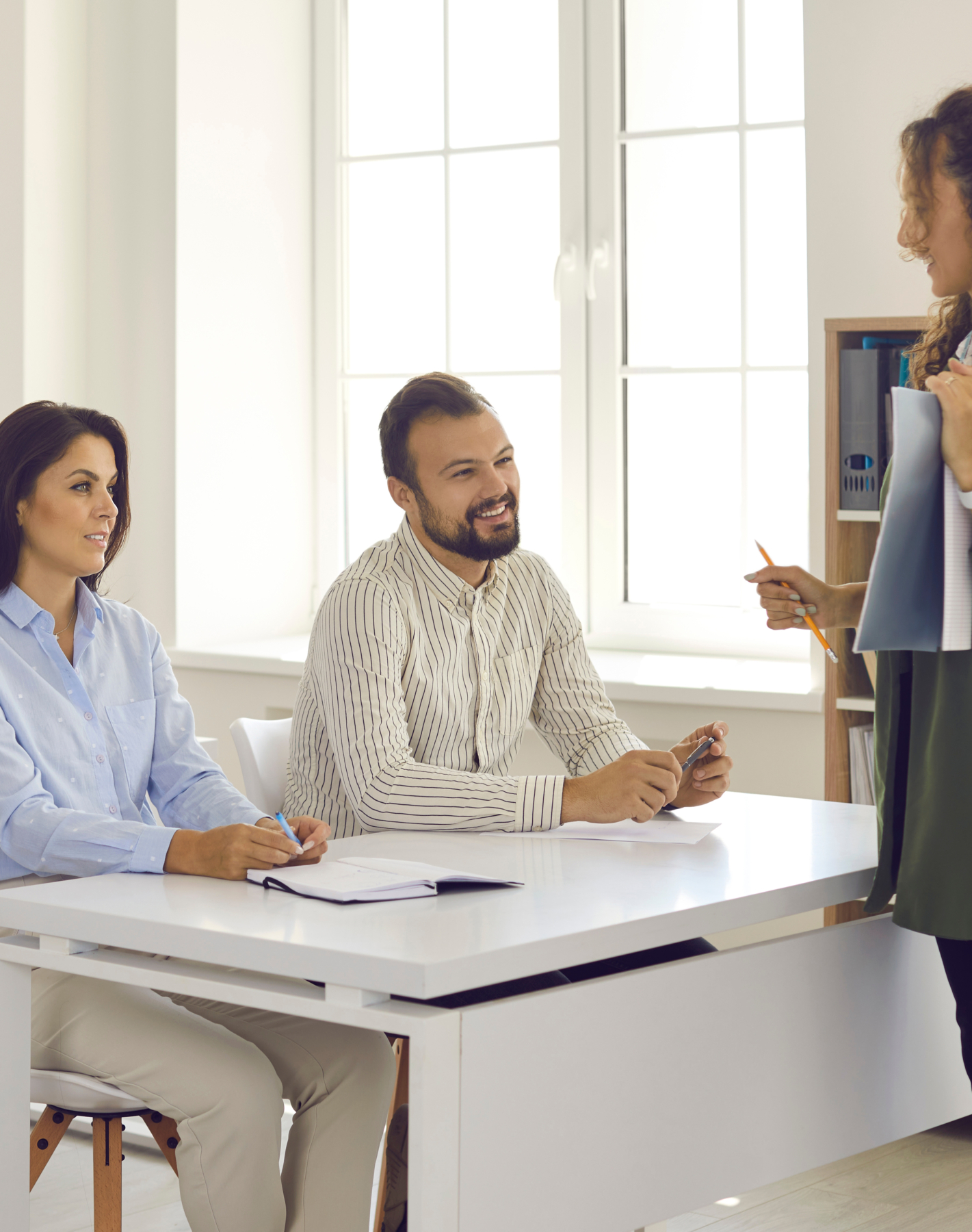 Der Bayerische Weg zur Fachkräftegewinnung – Ihre Chance auf eine pädagogische Karriere. Zwei junge Erwachsene sitzen auf einer Schulbank und werden von einer Lehrerin unterrichtet.