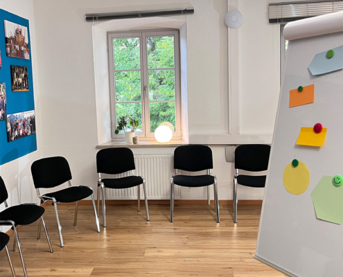 Kinderland Bildungsinstitut Impulskraft Konferenzraum mit Stühlen, hellem Parkettboden und einer Flipchart mit bunten Sticky-Notizen